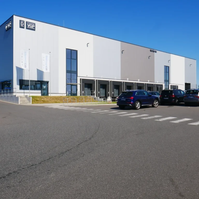 Moderne Lagerhalle mit großen Fenstern und Parkplatz im Vordergrund.